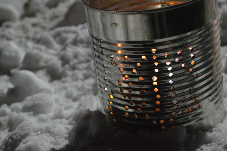A patterned tin-can lantern glowing in the snow