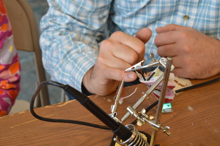 Hands assembling a small metal structure with a helping-hands tool